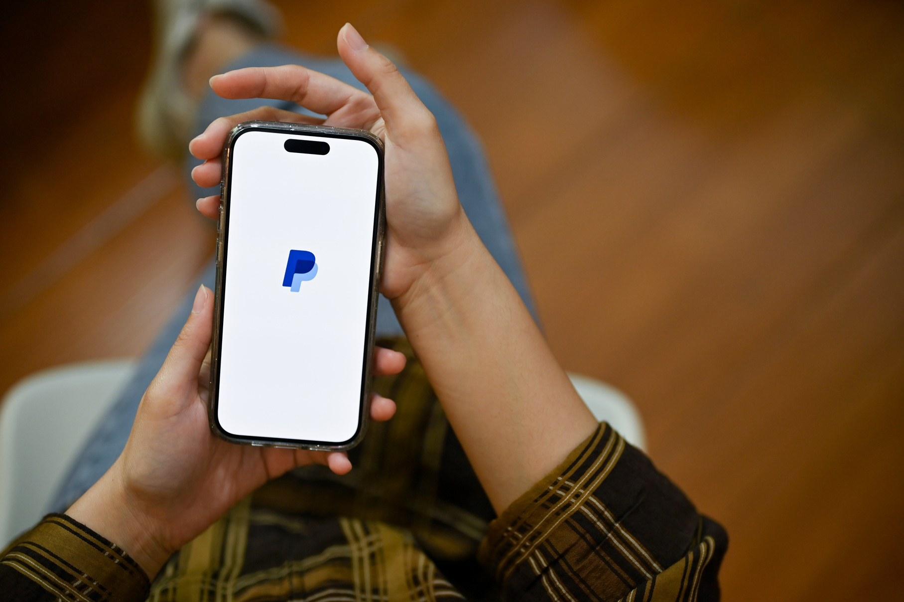 A female holding her smartphone with PayPal logo on screen. tran